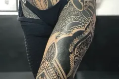 Una vista lateral de la cadera y el muslo de una persona con un tatuaje extenso de blackwork y estilo tribal. El diseño incluye un gran mandala ornamental en la cadera, formas geométricas marcadas y patrones detallados inspirados en lo polinesio que se extienden a lo largo de la pierna, con ropa interior negra alta de cintura. Tatuaje blackwork por Agu en Hipno Tattoo Estepona.