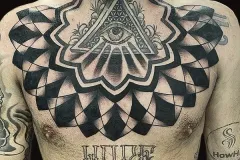 Una persona sin camisa muestra un gran tatuaje blackwork en el pecho, intrincado, con el Ojo de la Providencia dentro de un triángulo en el centro. El símbolo central está rodeado por un patrón geométrico complejo y simétrico, que se asemeja a un tablero de ajedrez distorsionado o a un mandala, y que se extiende por las clavículas. Debajo del diseño principal, la palabra “HOPE” está tatuada en una tipografía bold estilo gótico blackletter a lo largo del plexo solar. También se aprecian tatuajes adicionales en el cuello y los brazos. Tatuaje blackwork por Agu en Hipno Tattoo Estepona.