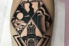 Un primer plano de una pierna con un tatuaje ilustrativo detallado en negro y gris, enmarcado dentro de una gran forma de rombo. El diseño incluye cuatro escenas distintas: un puente colgante suspendido, un paisaje con un sol y árboles, chimeneas industriales y un edificio grande con cúpula. La composición está rematada por una flor en plena floración y se sostiene en la parte inferior con un triángulo invertido y marcado. Tatuaje blackwork por Agu en Hipno Tattoo Estepona.