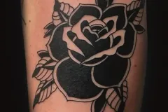 Un primer plano del brazo con un tatuaje bold de rosa en blackwork. El diseño neo-tradicional utiliza tinta negra sólida y espacio negativo para crear una pieza floral de alto contraste, con hojas afiladas y espinas. Tatuaje blackwork por Agu en Hipno Tattoo Estepona.