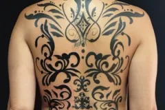 Tatuaje blackwork en espalda completa con diseño simétrico de florales decorativos, volutas y patrones geométricos. Tatuaje blackwork por Agu en Hipno Tattoo Estepona.