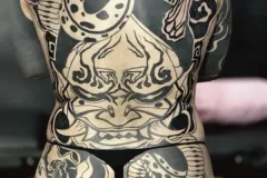 Tatuaje Oriental Noir completo en espalda y glúteos con demonio y serpiente, diseños simétricos y patrones geométricos. Tatuaje blackwork por Agu en Hipno Tattoo Estepona.